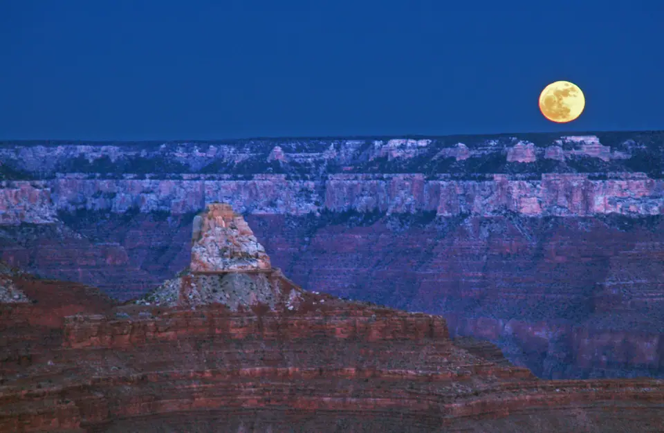 La Luna llena asomando sobre el horizonte del Gran Cañón, junto al borde rocoso que sirve de referencia visual